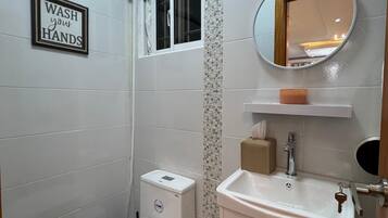 Une salle de bain avec des toilettes, un lavabo et un panneau indiquant : « Lavez-vous les mains ».