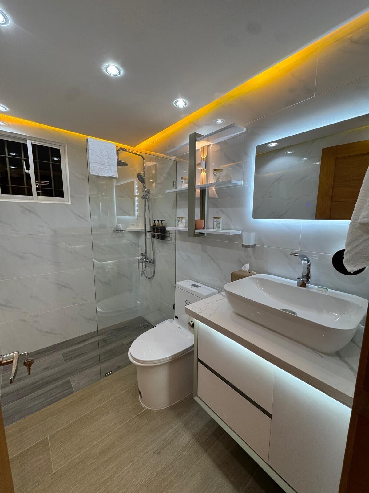 Un baño moderno con ducha acristalada, inodoro blanco y tocador con un espejo grande.