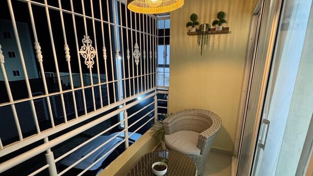 En balkon med fletmøbler, en hængende lampe og udsigt til bygninger i baggrunden.