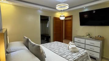 A bedroom with a bed, a dresser, a television, and a ceiling light fixture.