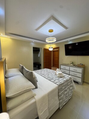 Un dormitorio con cama, cómoda, televisor y lámpara en el techo.