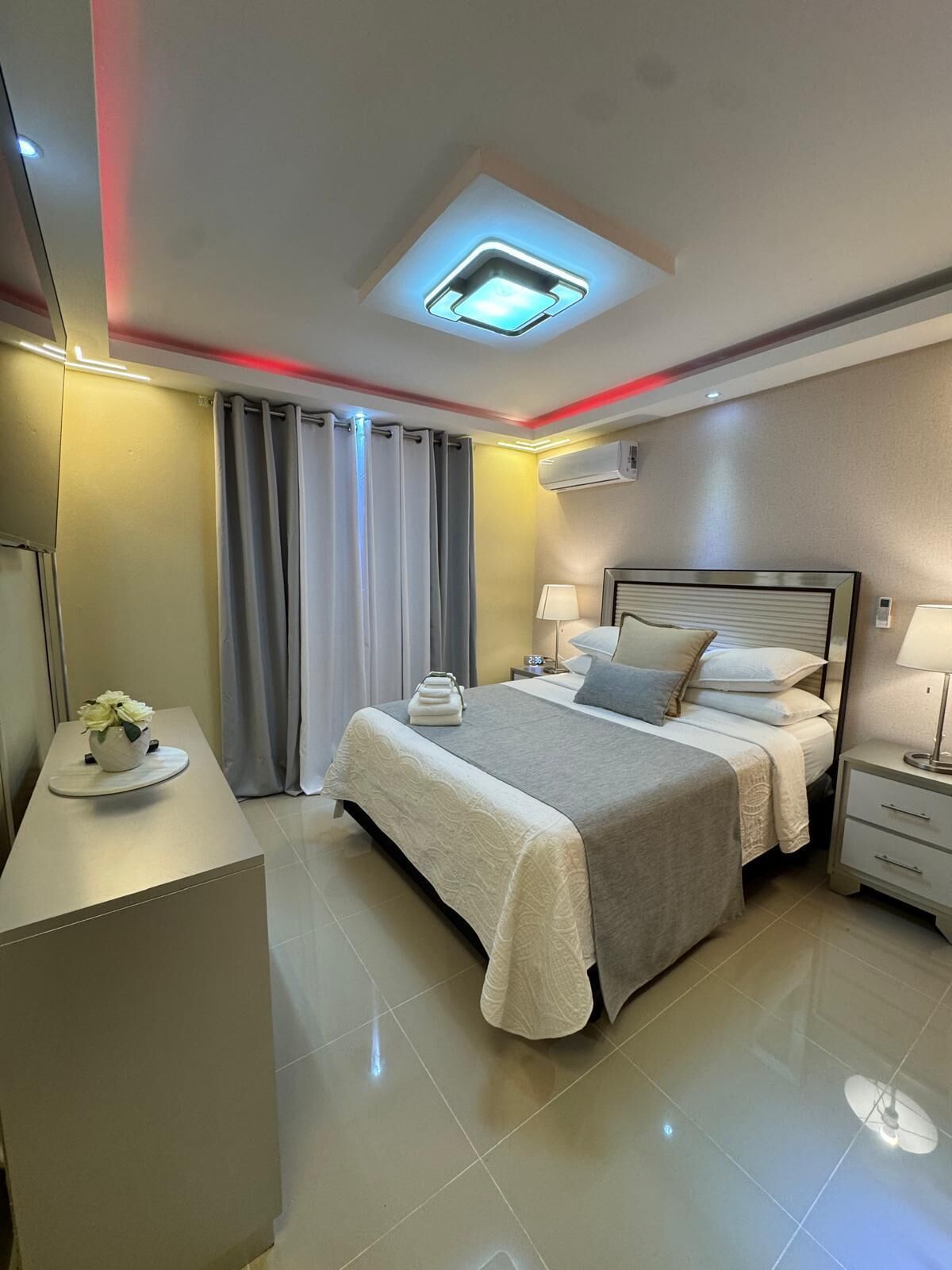 A modern hotel room with a bed, bedside tables, a desk, and a ceiling light fixture.