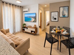 Ein modernes Wohnzimmer mit einem beigefarbenen Sofa, einem Esstisch mit Stühlen, einem Flachbildfernseher und einer wandmontierten Klimaanlage.