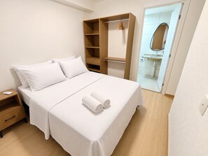 Ein ordentlich bezogenes Bett mit weißen Leinen, ein Nachttisch aus Holz und ein Kleiderschrank mit Platz zum Aufhängen.