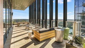 Een moderne buitenlounge met uitzicht op een stadsbeeld, ingericht met banken en stoelen, en een vloer met een patroon.