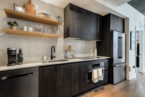 A modern kitchen with dark wood cabinets, a stainless steel refrigerator, and a coffee maker. - Luxury Lake View 23rd Fl Condo with Private Balcony & Rooftop Pool, Rainey St (Austin)
