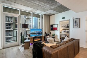 A modern living room with a leather sofa, a flat-screen TV, and a fireplace. - Luxury Lake View 23rd Fl Condo with Private Balcony & Rooftop Pool, Rainey St (Austin)