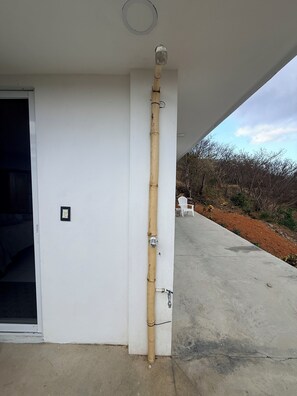 A bamboo pole attached to a white wall with a visible electrical outlet and a concrete floor. - Studio apartment with ocean view, minutes away from the beach, surf, & swimming! (San Juan del Sur)