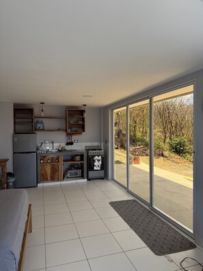 A modern kitchen with a built-in oven, a refrigerator, and a microwave. There is a large sliding glass door leading to an outdoor area. - Studio apartment with ocean view, minutes away from the beach, surf, & swimming! (San Juan del Sur)