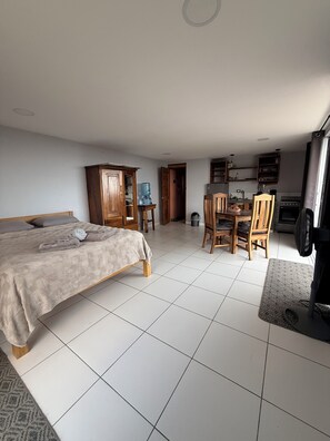 A bedroom with a bed, a wooden wardrobe, a desk with chairs, and a kitchenette area. - Studio apartment with ocean view, minutes away from the beach, surf, & swimming! (San Juan del Sur)