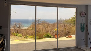 Ein Zimmer mit einer großen Glasschiebetür, die auf einen Balkon mit Blick auf das Meer und Bäume führt.