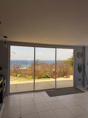 A room with a large sliding glass door leading to a balcony with a view of the ocean and trees. - Studio apartment with ocean view, minutes away from the beach, surf, & swimming! (San Juan del Sur)