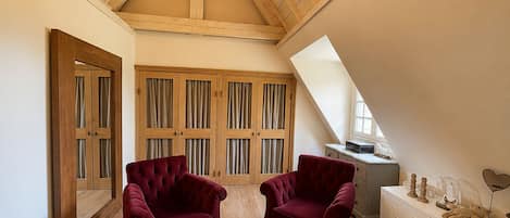 Une pièce avec des poutres apparentes en bois au plafond, une grande fenêtre et une armoire fermée par des rideaux.
