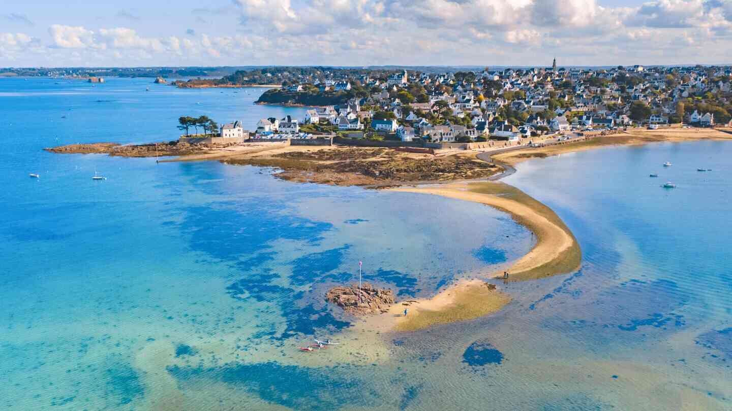An aerial view of a coastal town with clear blue waters, sandy beaches, and residential buildings.