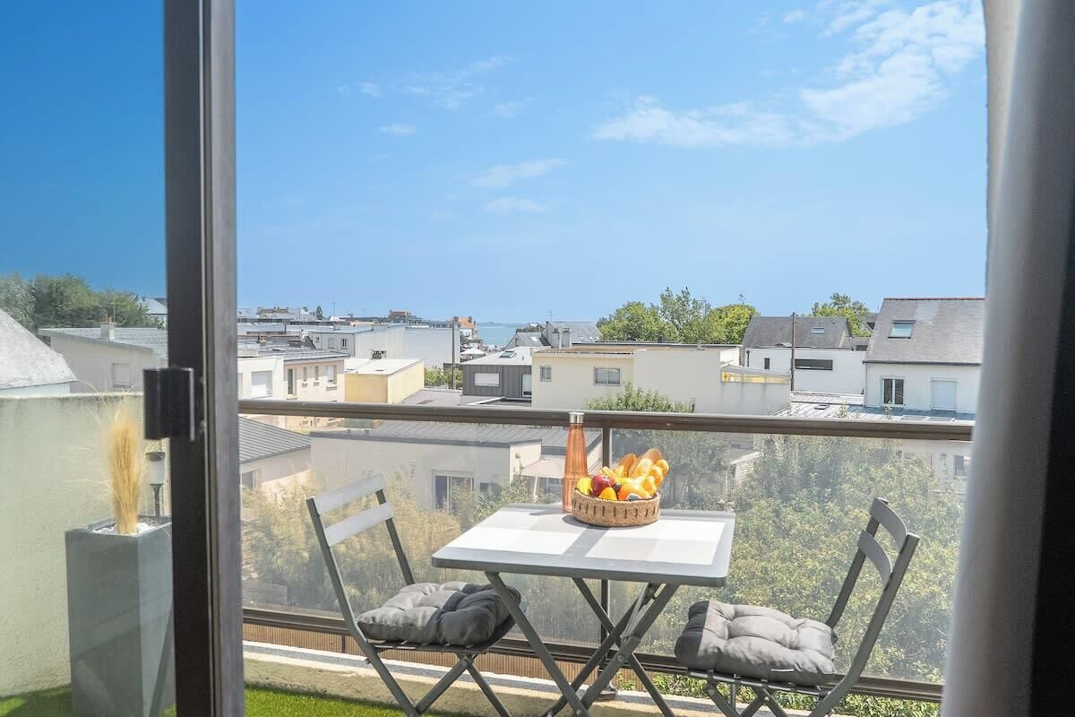 A balcony with a table and chairs, a basket of fruit, and a view of the cityscape.