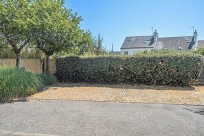 A paved driveway leading to a property with a hedge and a tree. - T2 avec aperçu mer, plage et commerces à pied (Larmor-Plage)