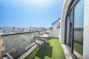 A balcony with a table and chairs, a small garden area, and a view of the neighborhood. - T2 avec aperçu mer, plage et commerces à pied (Larmor-Plage)