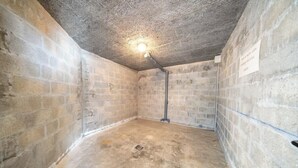 Een kamer met bakstenen muren, een betonnen vloer en één lamp aan het plafond.