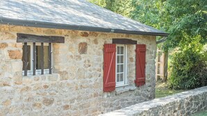 Un bâtiment en pierre avec un toit en pente et une fenêtre ornée de volets rouges.