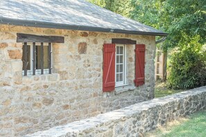 Ein Steinhaus mit geneigtem Dach und einem Fenster mit roten Rollläden.