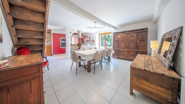 Un vaste espace à manger avec une grande table et des chaises, un escalier en bois et une cuisine en arrière-plan.