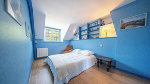 Une chambre à coucher comprenant un lit, une chaise, une petite table et des étagères ornées d’objets décoratifs.