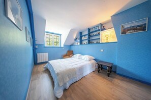 Ein Schlafzimmer mit einem Bett, einem Sessel, einem kleinen Tisch und Regalen mit Dekoration.