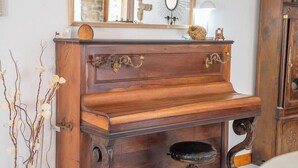 Un piano en bois, orné de sculptures complexes et agrémenté de détails en laiton, est placé contre un mur, devant lequel se trouve un miroir reflétant un décor rustique.