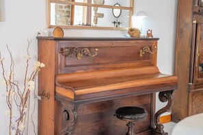 Ein Holzpiano mit aufwendigen Schnitzereien und Messingakzenten, platziert vor einer Wand, deren Spiegel eine rustikale Einrichtung reflektiert.