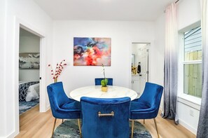 A dining area with a round table, blue chairs, a vase with flowers, and a colorful abstract painting on the wall. - Newly Built 3BR/3BA: Easy Access to Downtown, IAH, NRG, Med Center & Heights (Houston)