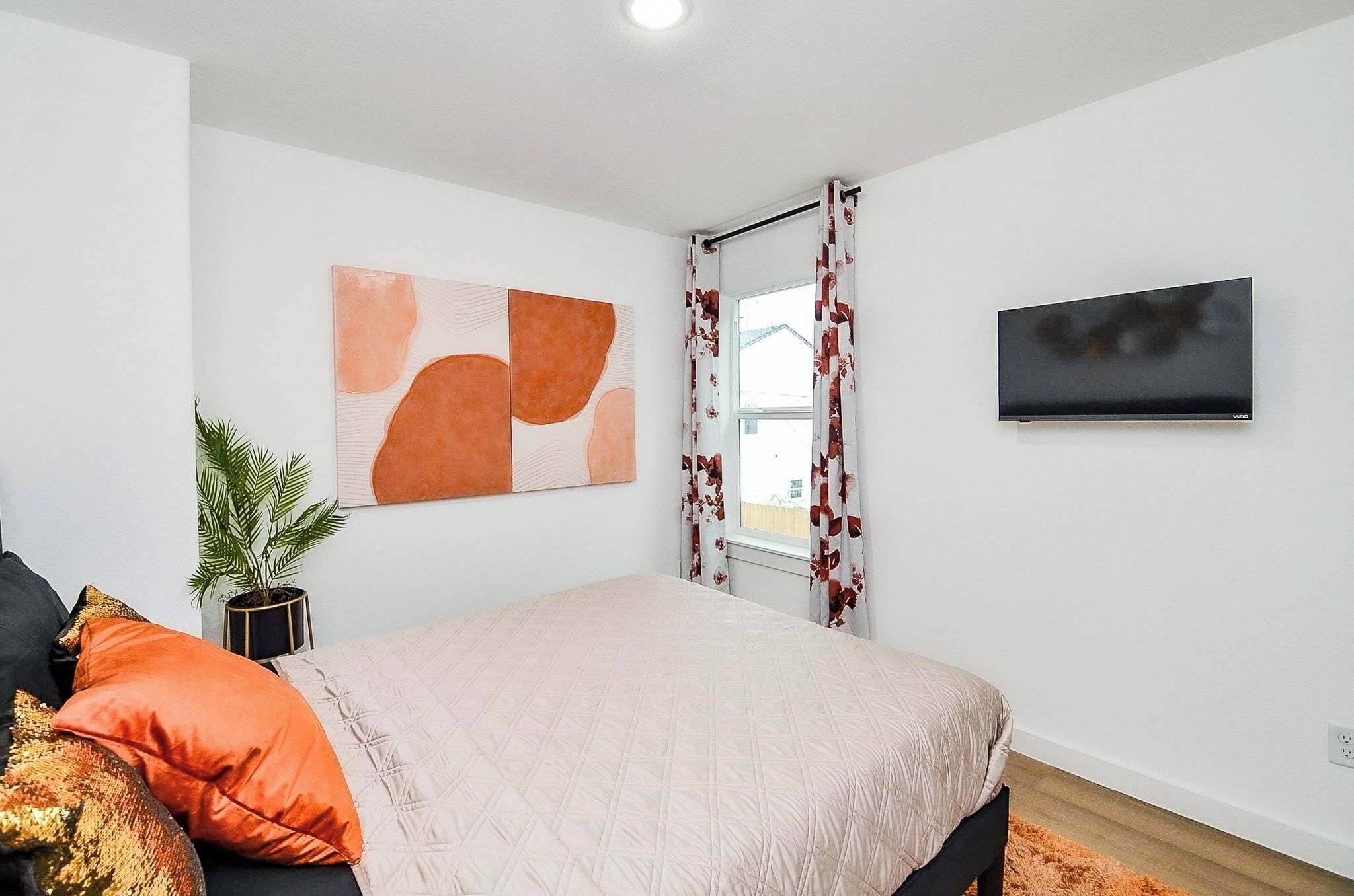 A bedroom with a bed, a TV, a window with curtains, and a painting on the wall.