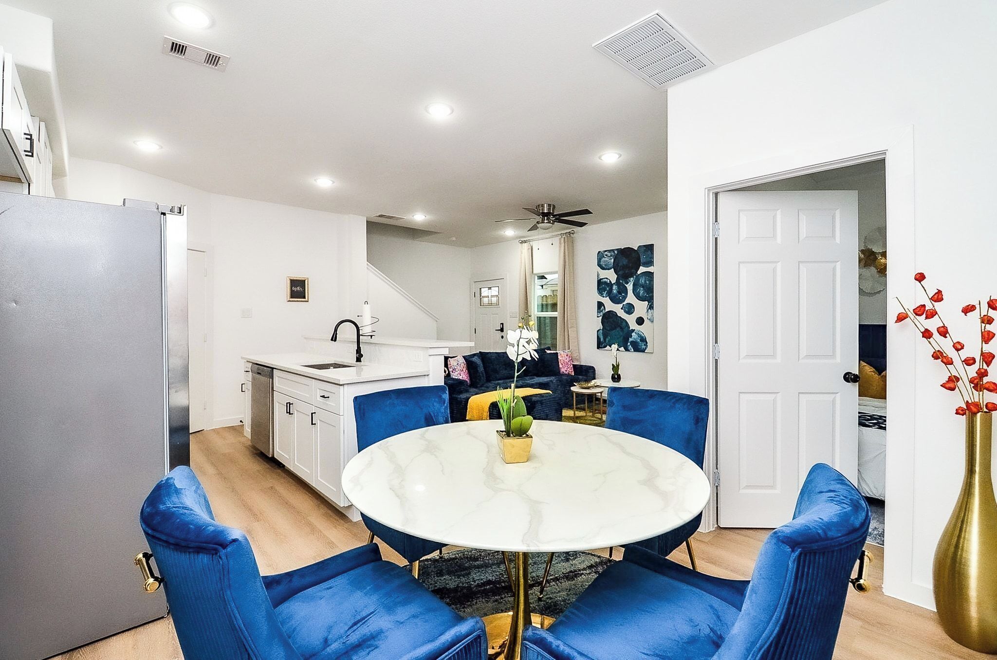 A modern kitchen with white cabinets, a black faucet, and a white marble dining table with blue upholstered chairs.