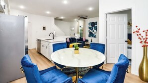 Uma cozinha moderna com armários brancos, uma torneira preta e uma mesa de jantar de mármore branco com cadeiras estofadas em azul.