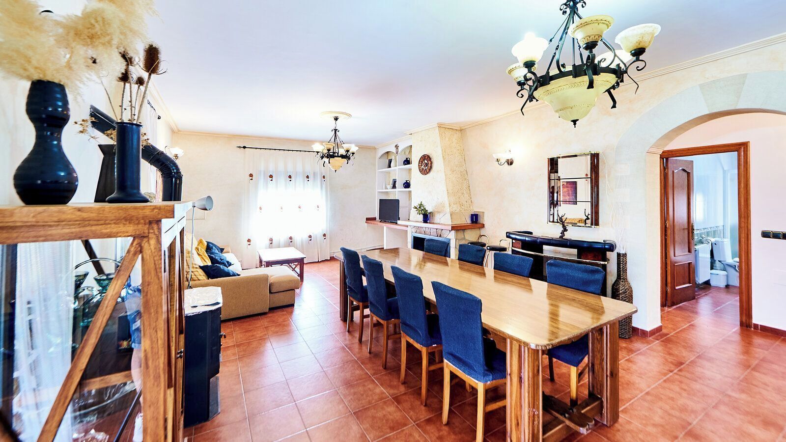 A spacious living area with a dining table, blue chairs, and a sofa.