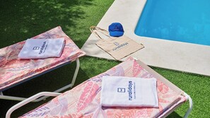 Two lounge chairs with towels and a bag with the logo 'ruraldays' on a grassy area beside a pool.