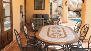 An outdoor patio with a round table and chairs, a sofa, and a view of a swimming pool.