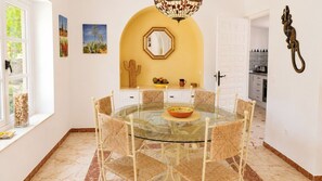 A dining area with a glass table surrounded by woven chairs, a cacti decoration, and a mirror above the table.