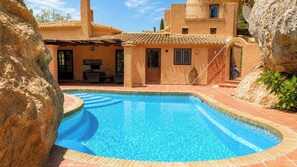 A swimming pool with a tiled edge, surrounded by a building with a tiled roof and a stone wall.