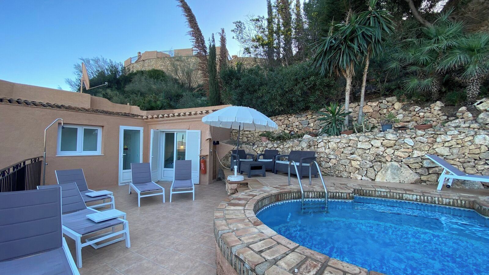 A swimming pool with lounge chairs and a stone wall.