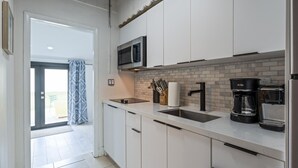 Een moderne keuken met witte kastjes, een zwarte magnetron, een koffiezetapparaat en een betegelde spatwand.
