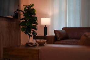 Ein gemütliches Wohnzimmer mit einem braunen Sofa, einem Beistelltisch, einer Lampe und einer großen Zimmerpflanze.