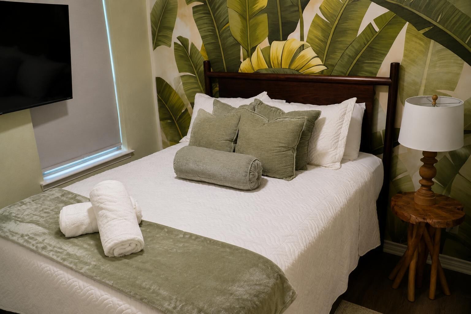 A neatly made bed with pillows and a blanket, a bedside lamp, and a wall with a large leaf pattern.