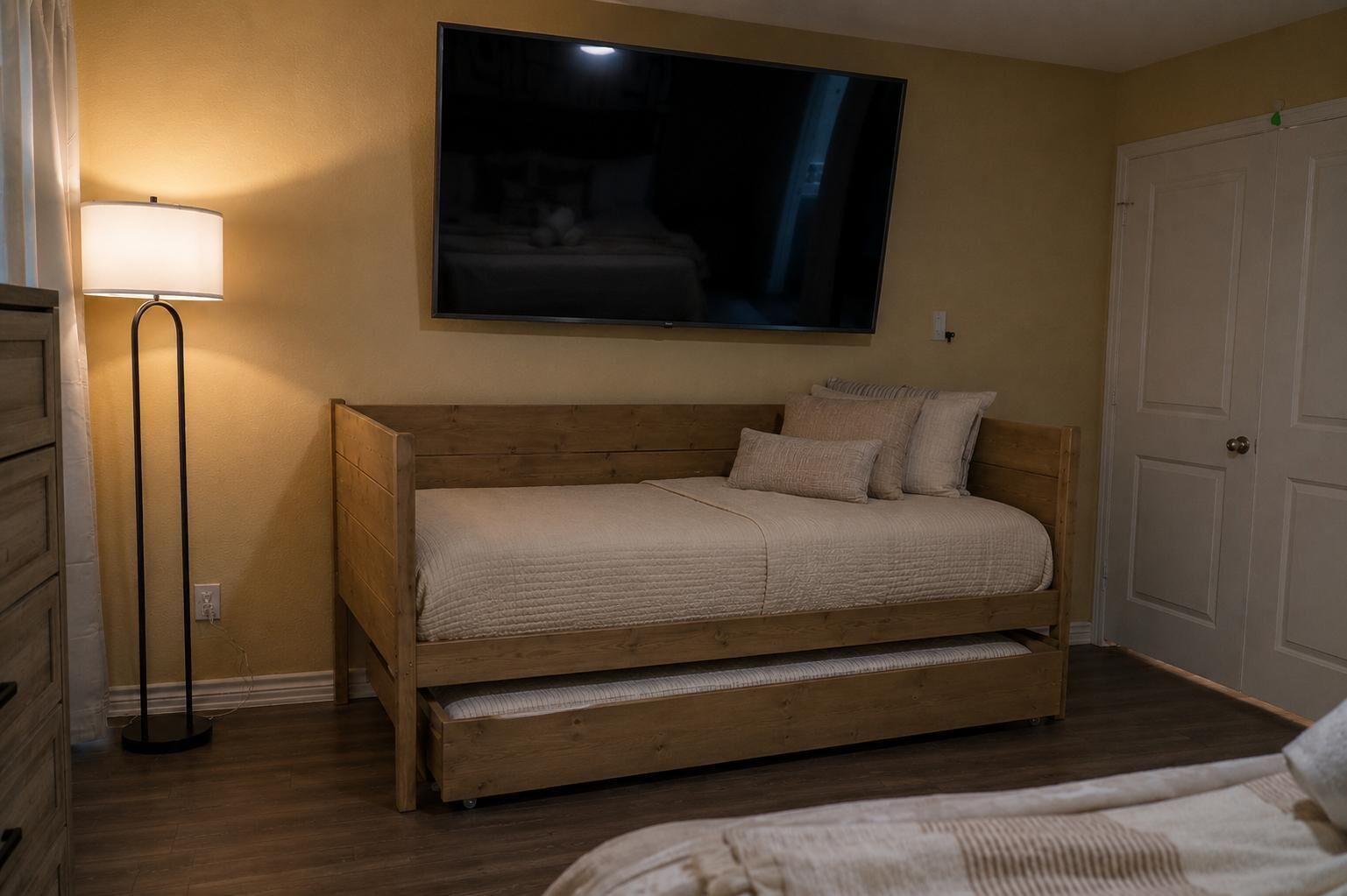 Ein Schlafzimmer mit einem Holzbett, einer Nachttischlampe, einem an der Wand montierten Fernseher und einer Tür.