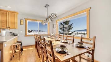 Uma sala de jantar com mesa de madeira posta para quatro pessoas, cadeiras de madeira e vista para uma paisagem nevada através de grandes janelas.