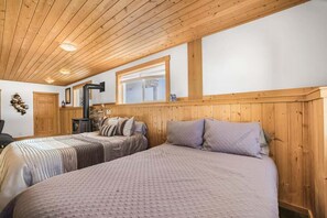 Une chambre confortable avec deux lits, des poutres apparentes en bois au plafond, une cheminée et une fenêtre.