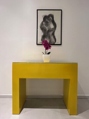 A yellow table with a white vase containing purple flowers, positioned against a plain wall with a black and white artwork above. - The Palm, Beachfront Home in Playa Hermosa, Jaco, Costa Rica. Prime location (Playa Hermosa)