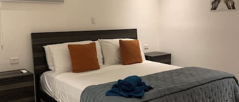 A bedroom with a bed, a nightstand, a chair, a ceiling fan, and a painting on the wall.