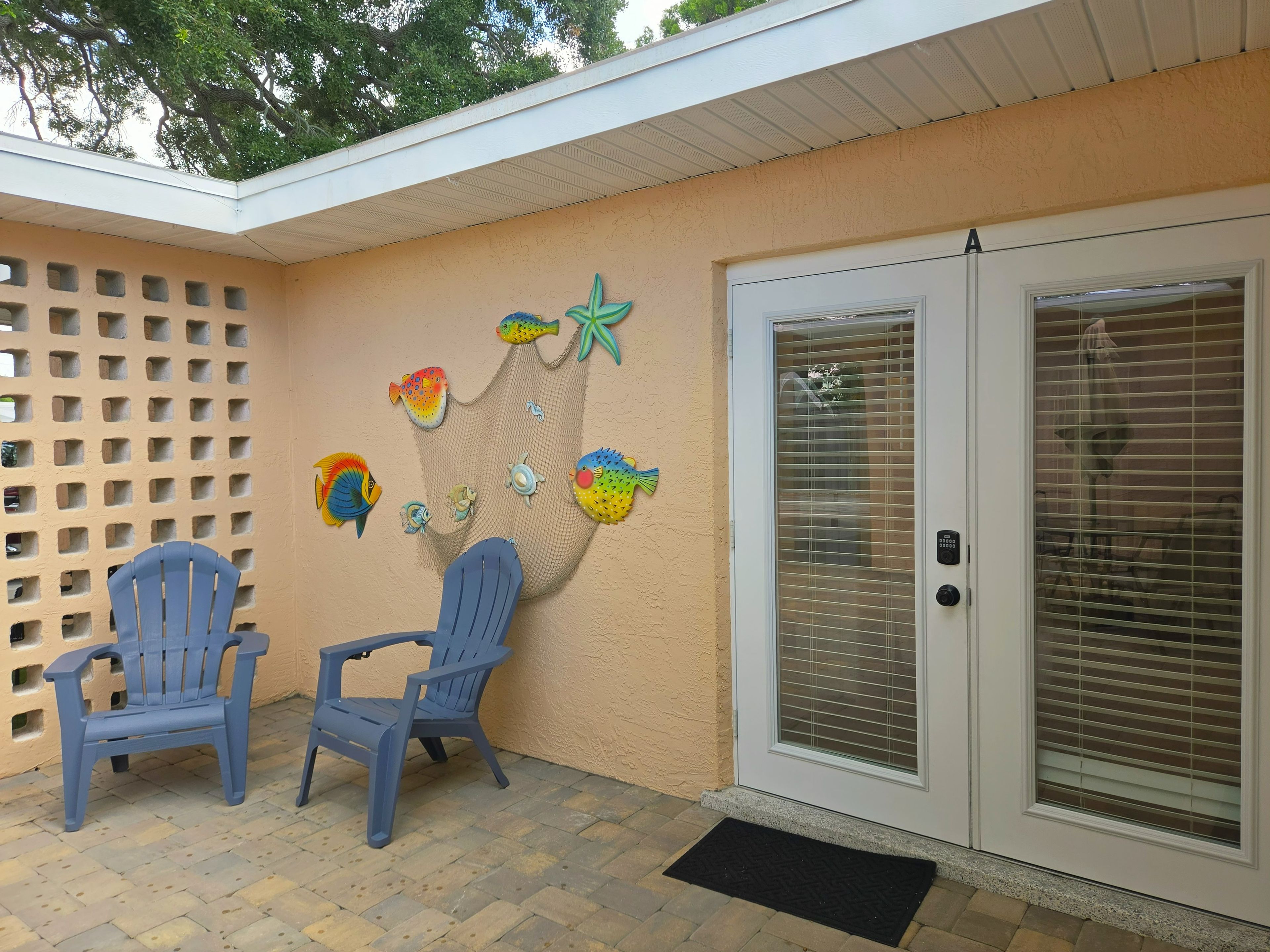 Un patio con dos sillas azules, una pared decorada con peces y estrellas de mar, y un ventanal corredizo.