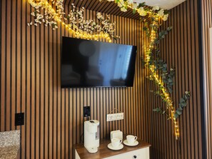 Een moderne kamer met een flatscreen televisie aan een houten wand, een koffiezetapparaat en twee kopjes op een houten tafel.