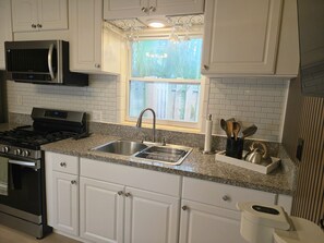 A kitchen with white cabinets, a stainless steel sink, a microwave, and a stove. - Family Nest Romantic Stay-Memories (Bradenton)